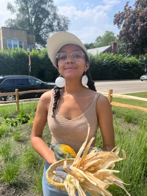 Indigenous Person with braids and earrings holding corn and squash 