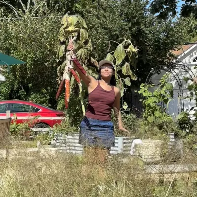 Person in a hat and brown tank top holding up colorful corn in front of native grasses