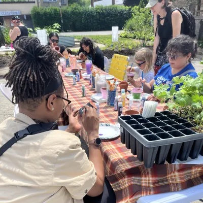 People at a long table with plants on it, painting flower pots
