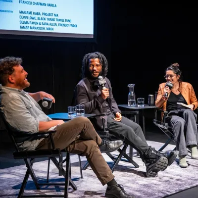 Three people sitting on a stage with microphones, talking to each other at an event.