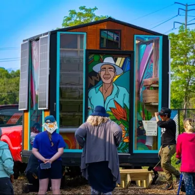 Several people checking out the Healing House, a small house on wheels with brightly colored murals and solar panels. This was created as part of Earth Art Chicago.